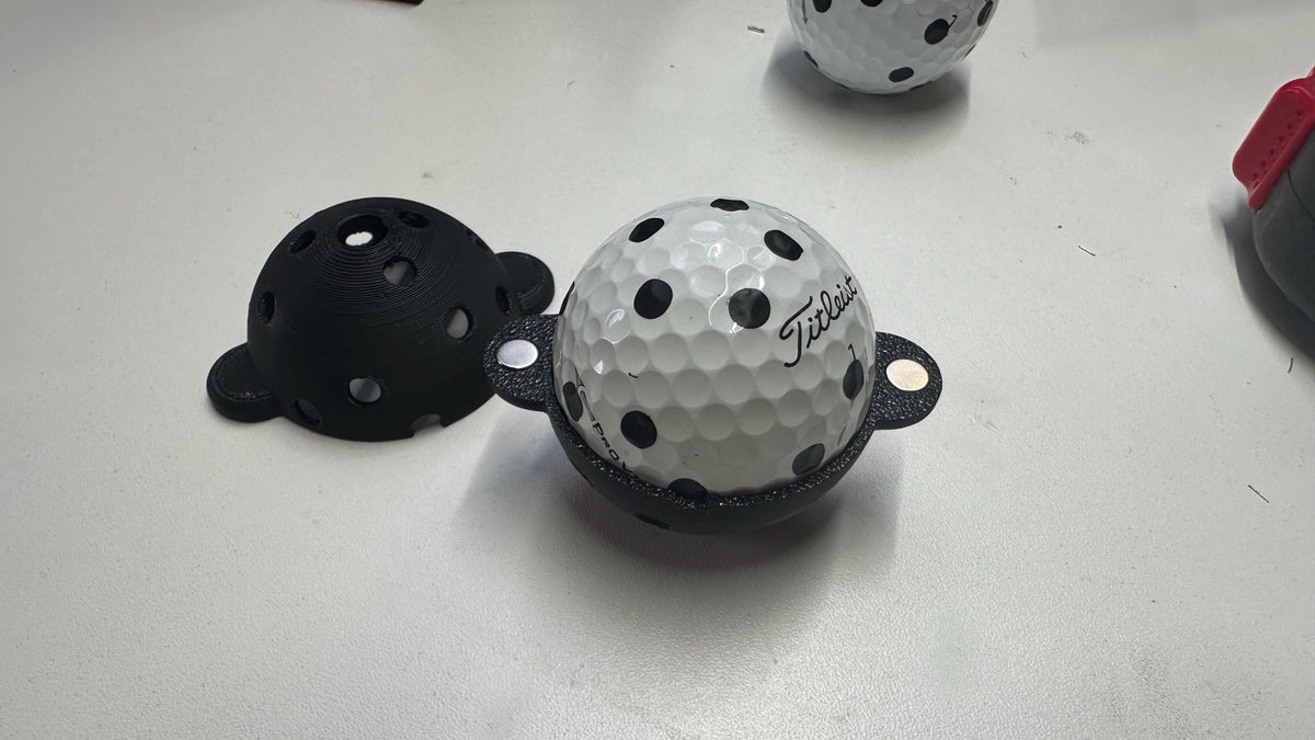 Square Golf ball marker opened around a golf ball with black markings