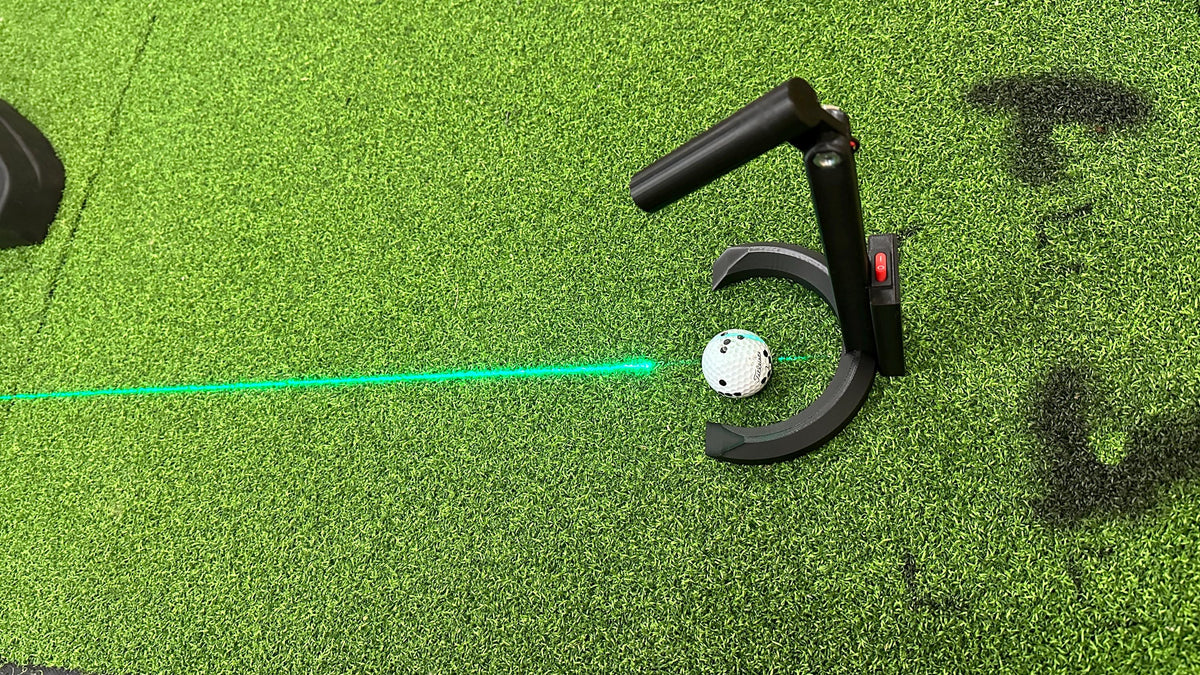 Golf ball beside the laser tool projecting a green target line across the mat
