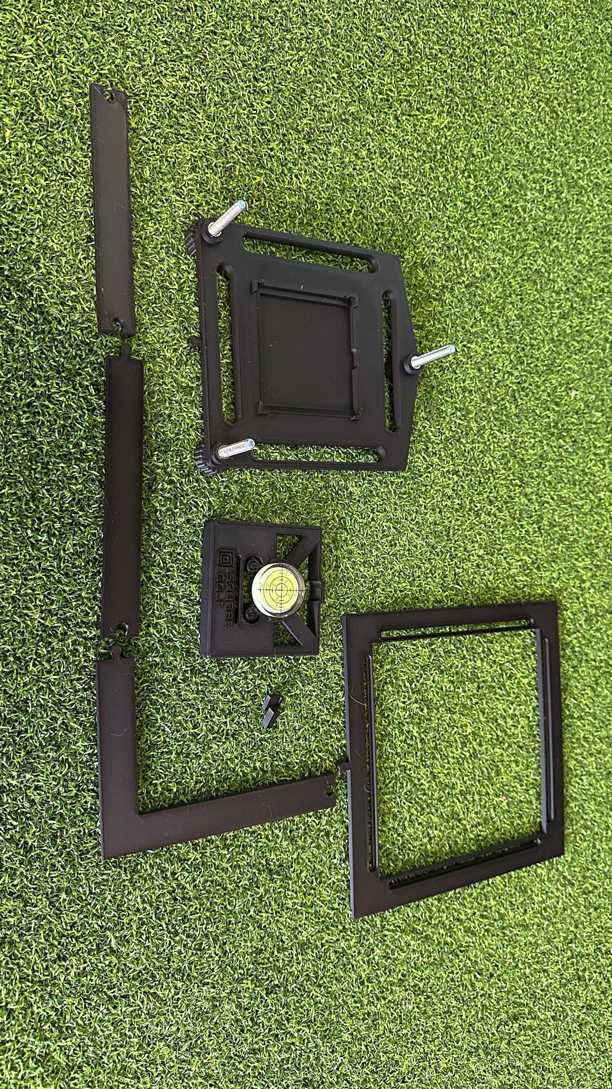 Square Golf alignment system components laid out: adjustable base, bubble level and ball positioning frame