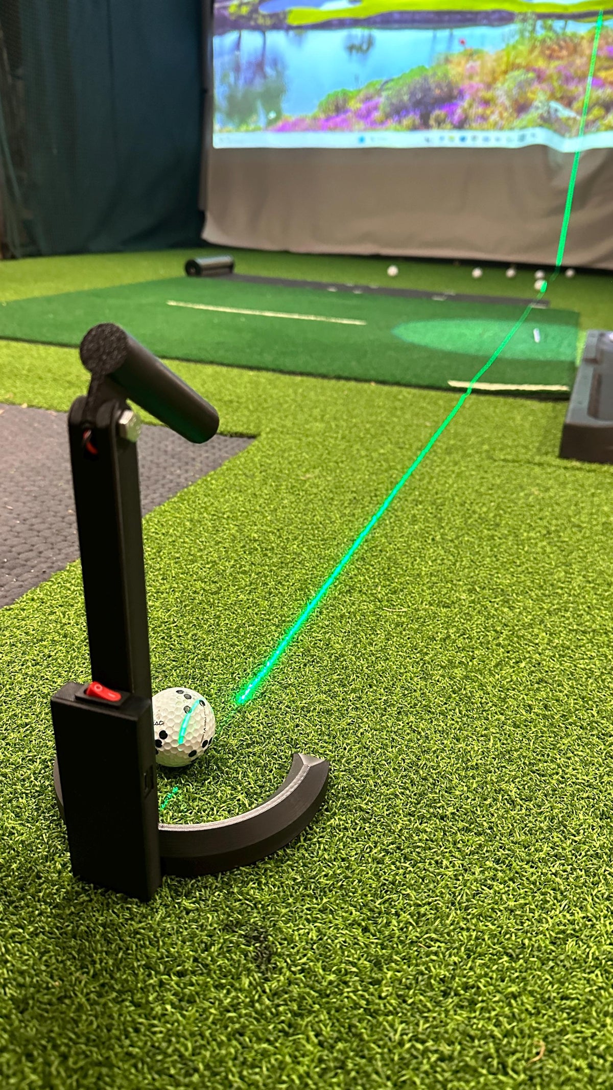 Laser alignment and putting aid projecting a green line across the golf mat beside a golf ball